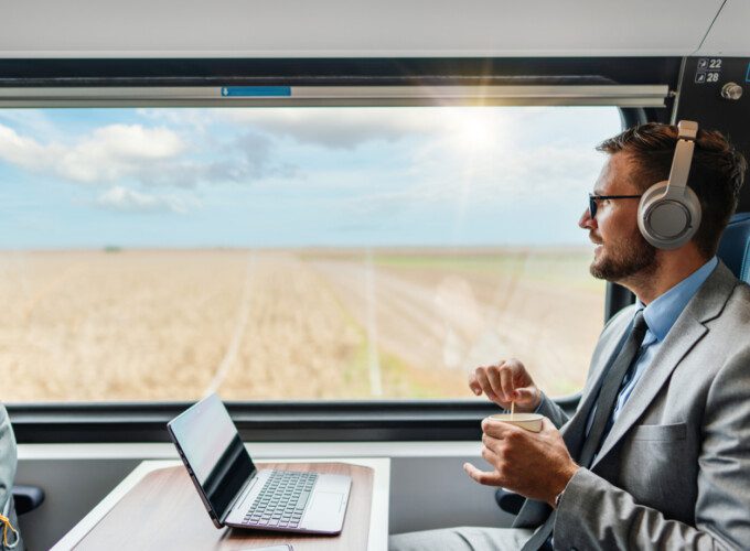 hospitality p experience A male passenger wearing headphones works on a laptop while enjoying a coffee on his journey.